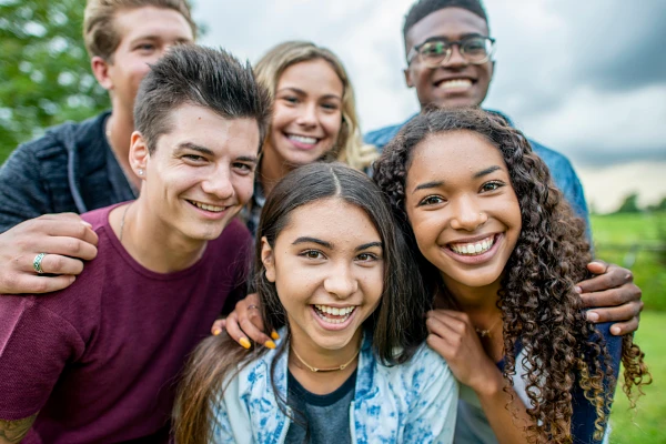 A group of six young people are smiling and posing cheerfully outdoors.