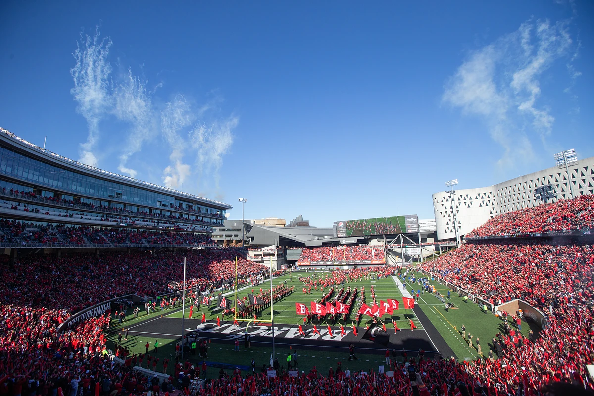 A large crowd fills Nippert stadium during a lively football game with clear blue skies above.