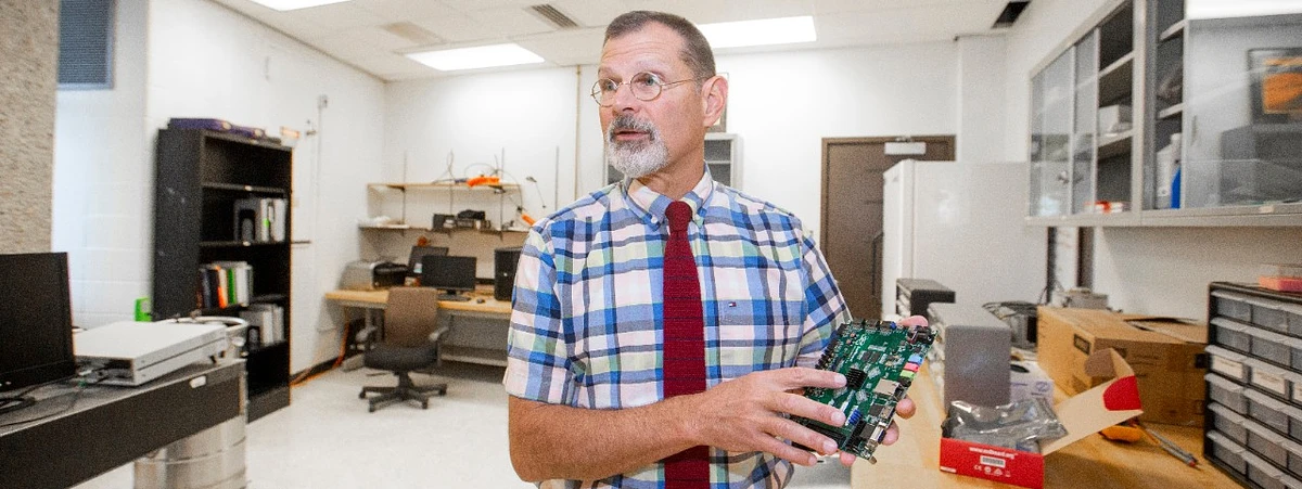 A professor holds a circuit board and speaks to a class