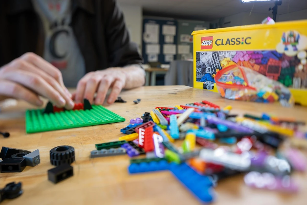 A person is assembling a structure with LEGO pieces on a table with a LEGO Classic box nearby.