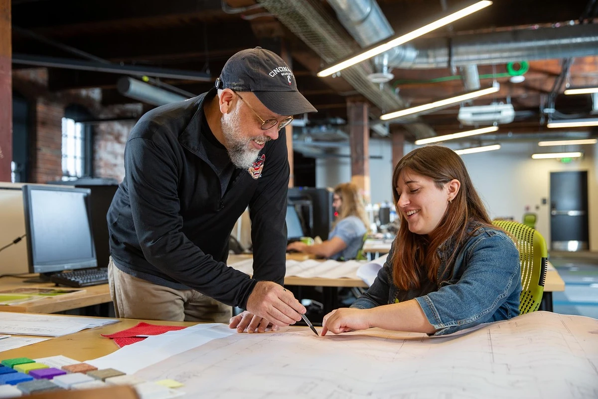 Two people are collaborating on a project at a table in an open-plan office.
