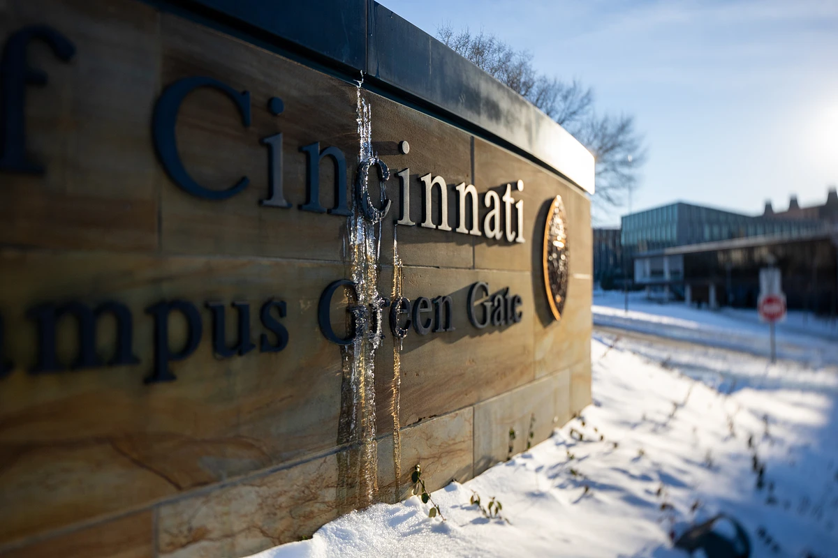 A sign for the "Campus Green Gate" at the University of Cincinnati is adorned with icicles in a snowy landscape.