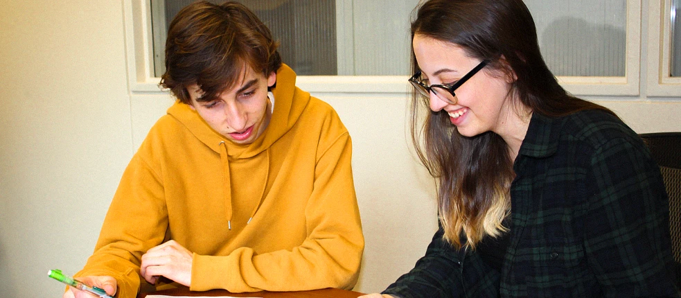 Student smiles while tutoring another student at a table