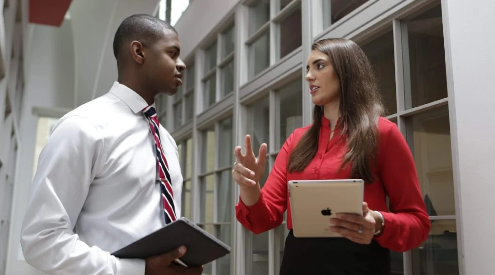 Two professionally-dressed students talking in the hall while holding tablet computers